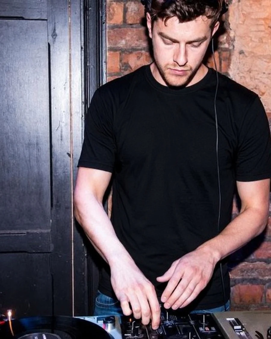 CAFE HAUS DJ playing on decks beside an exposed brick wall